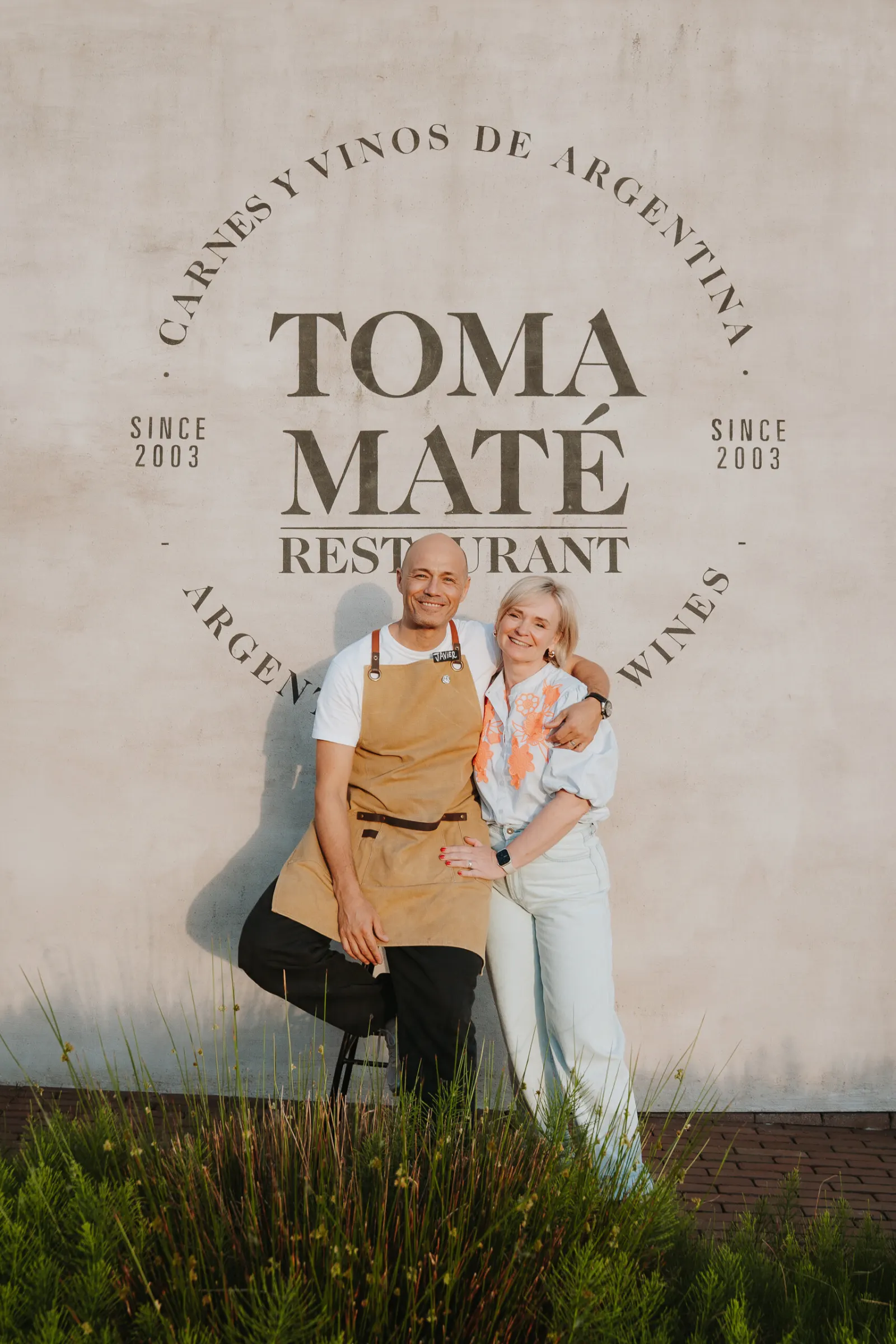 De gastheer en gastvrouw van Toma Maté voor het logo op de muur