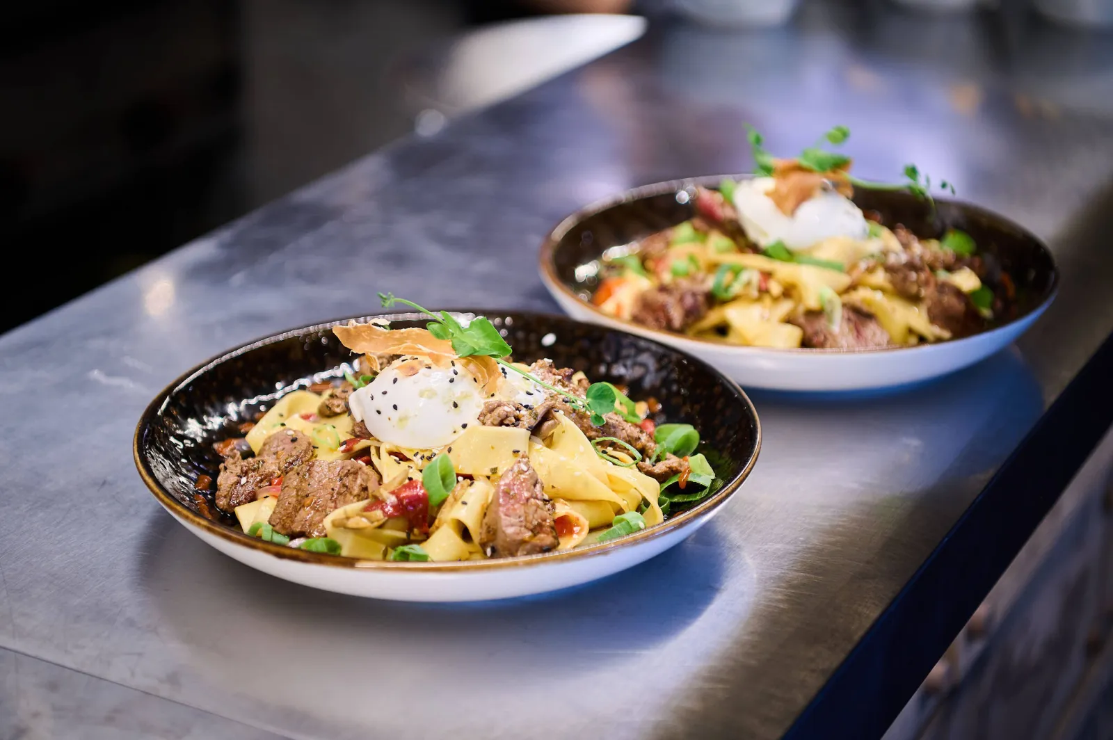 Twee borden brede pasta met stukjes rundvlees op de keukentoog