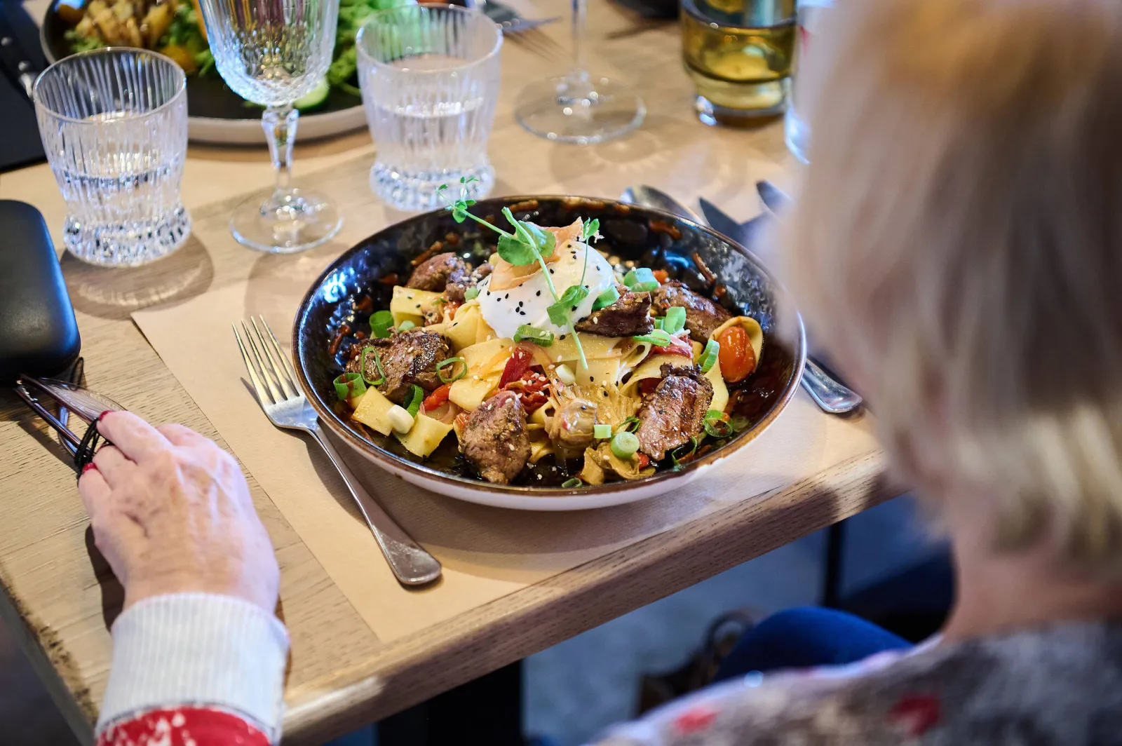 Een gaste aan tafel voor een bord pasta met rundvlees