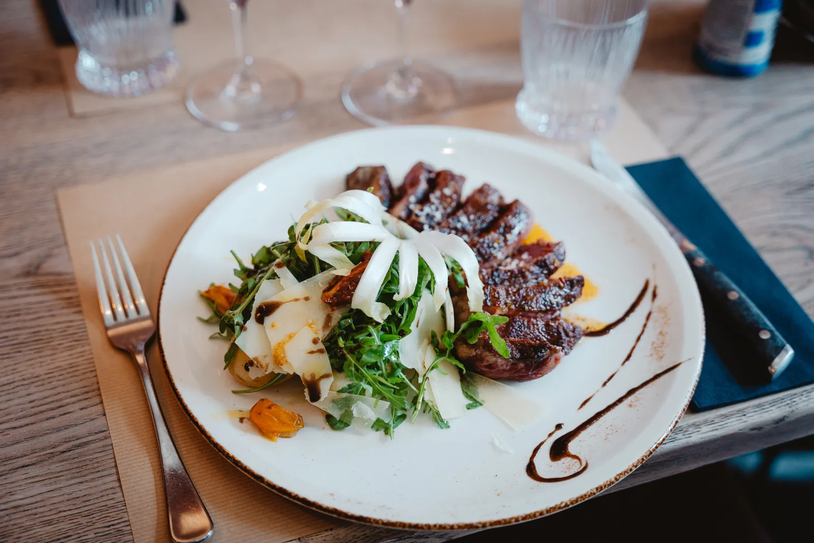 Gesneden gegrild rundvlees met rucola en Parmezaanse schilfers op een wit bord