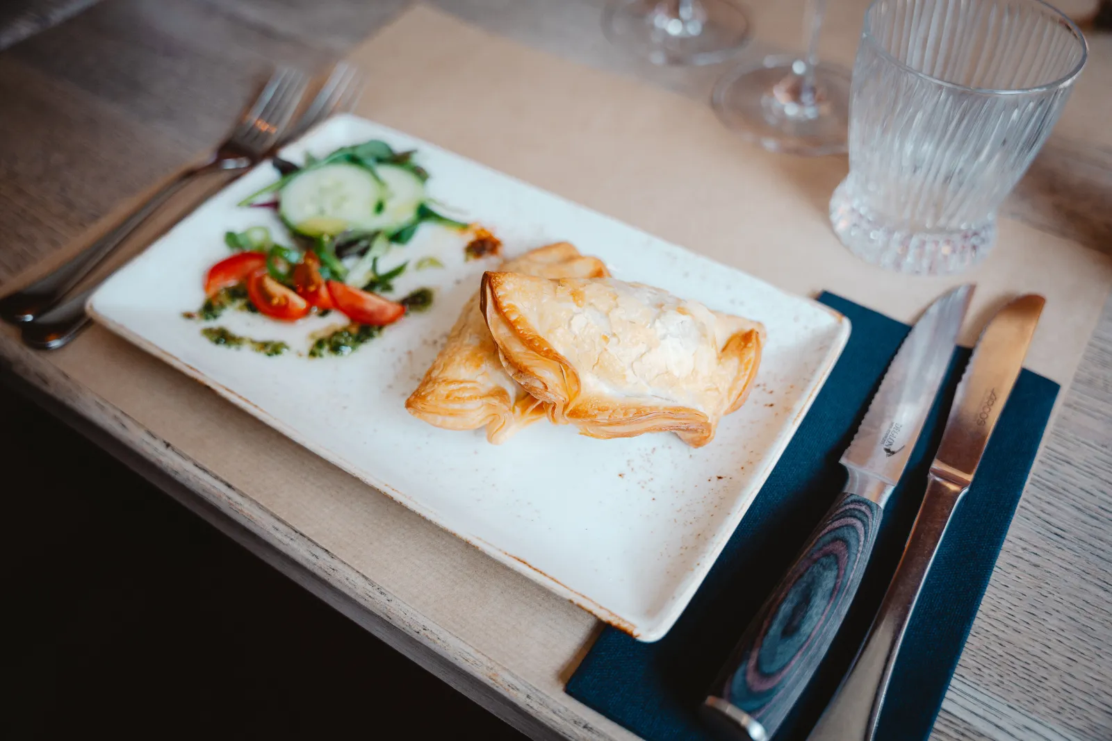 Gevouwen deegpakketje met een kleine salade op een rechthoekig bord