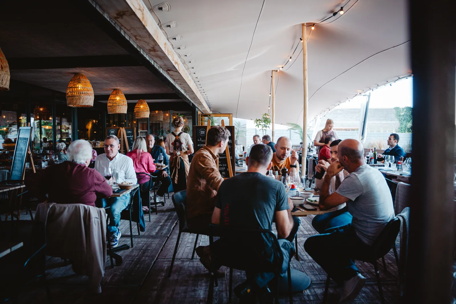 Gasten aan tafel op het volle overdekte terras met rotan lampen