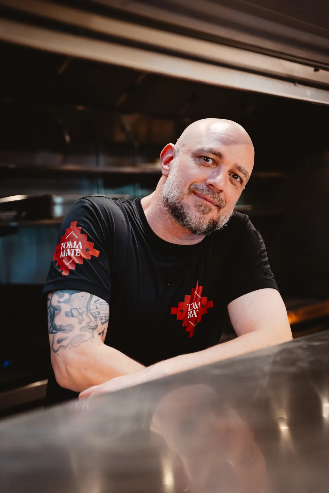 De chef in zwart Toma Maté-shirt leunt op de keukentoog