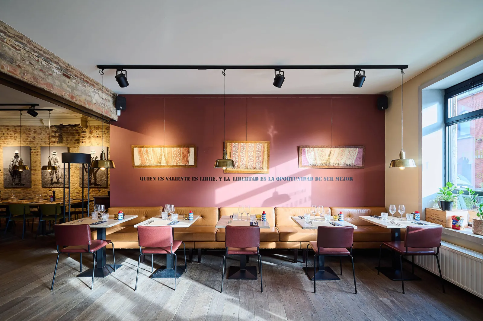 Eetzaal met lange bank, roze stoelen en tekst op een rode muur