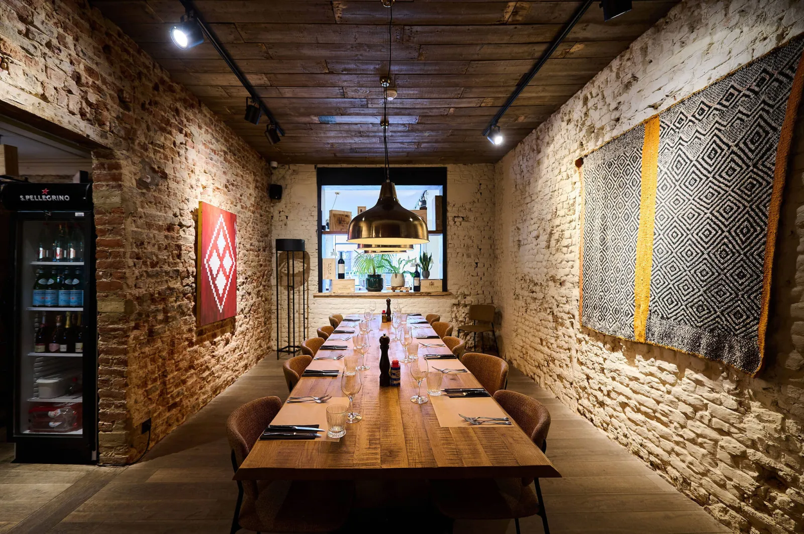 Lange houten tafel in een zaal met bakstenen muren en wandkleden