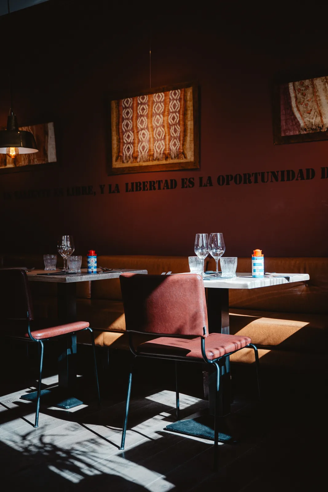 Gedekte tafels en een roze stoel in het zonlicht tegen een rode muur