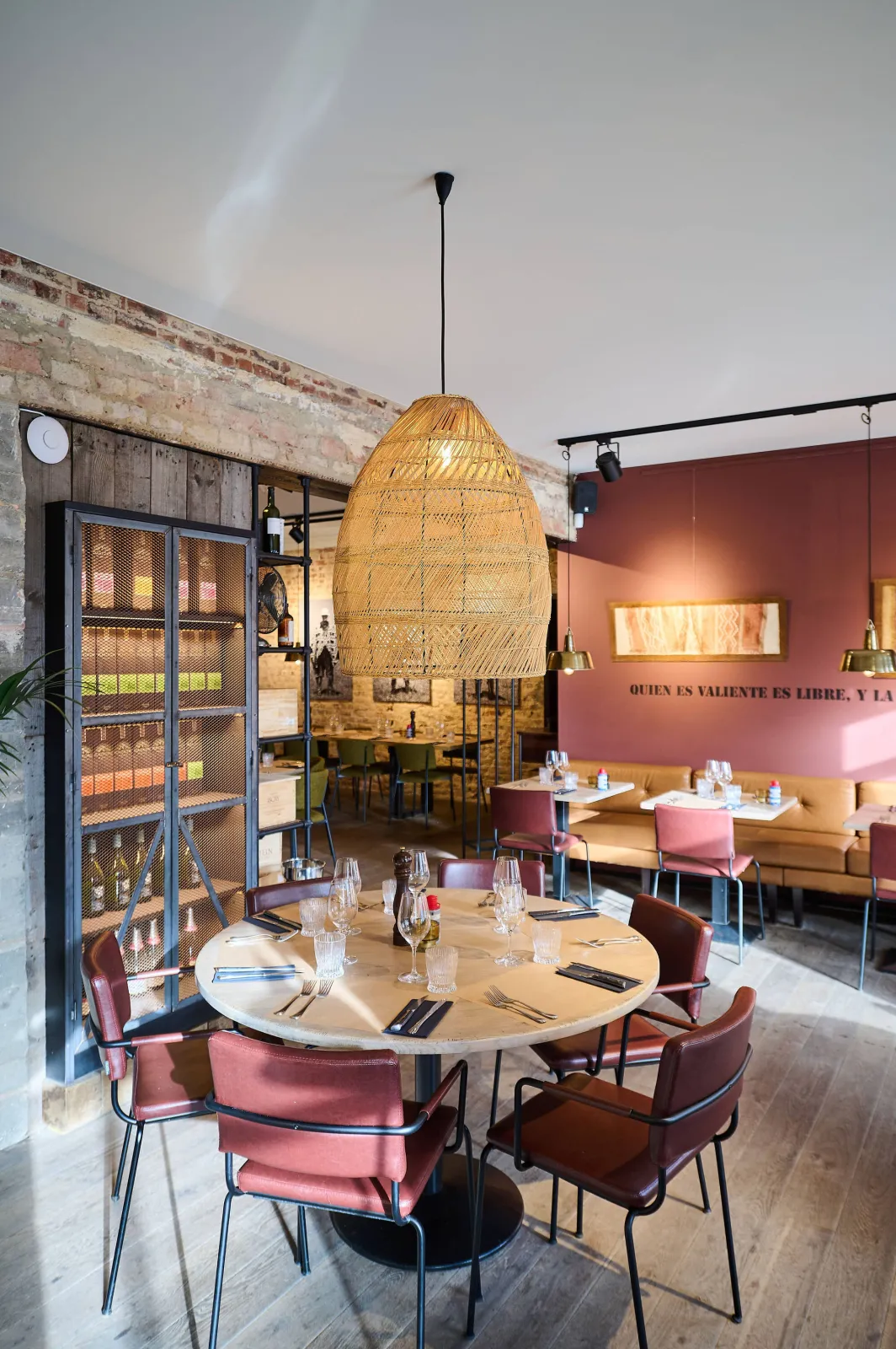 Ronde tafel met roze stoelen onder een grote rotan hanglamp