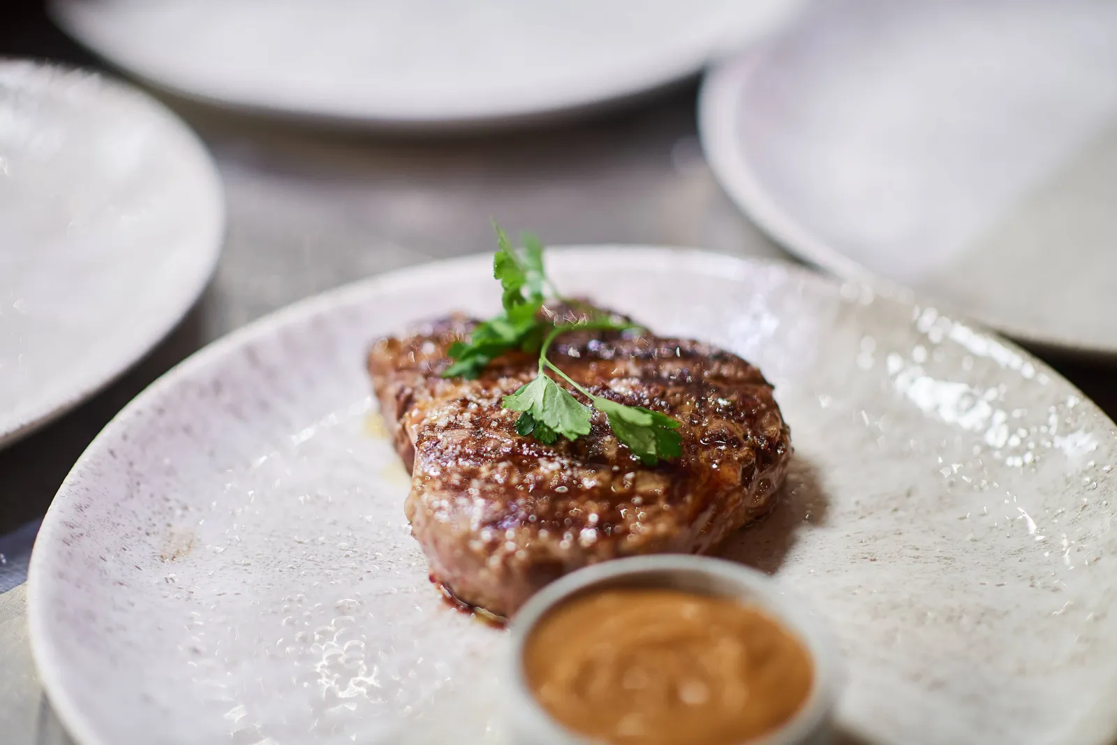 Gegrilde steak met kruiden en een potje saus op een wit bord