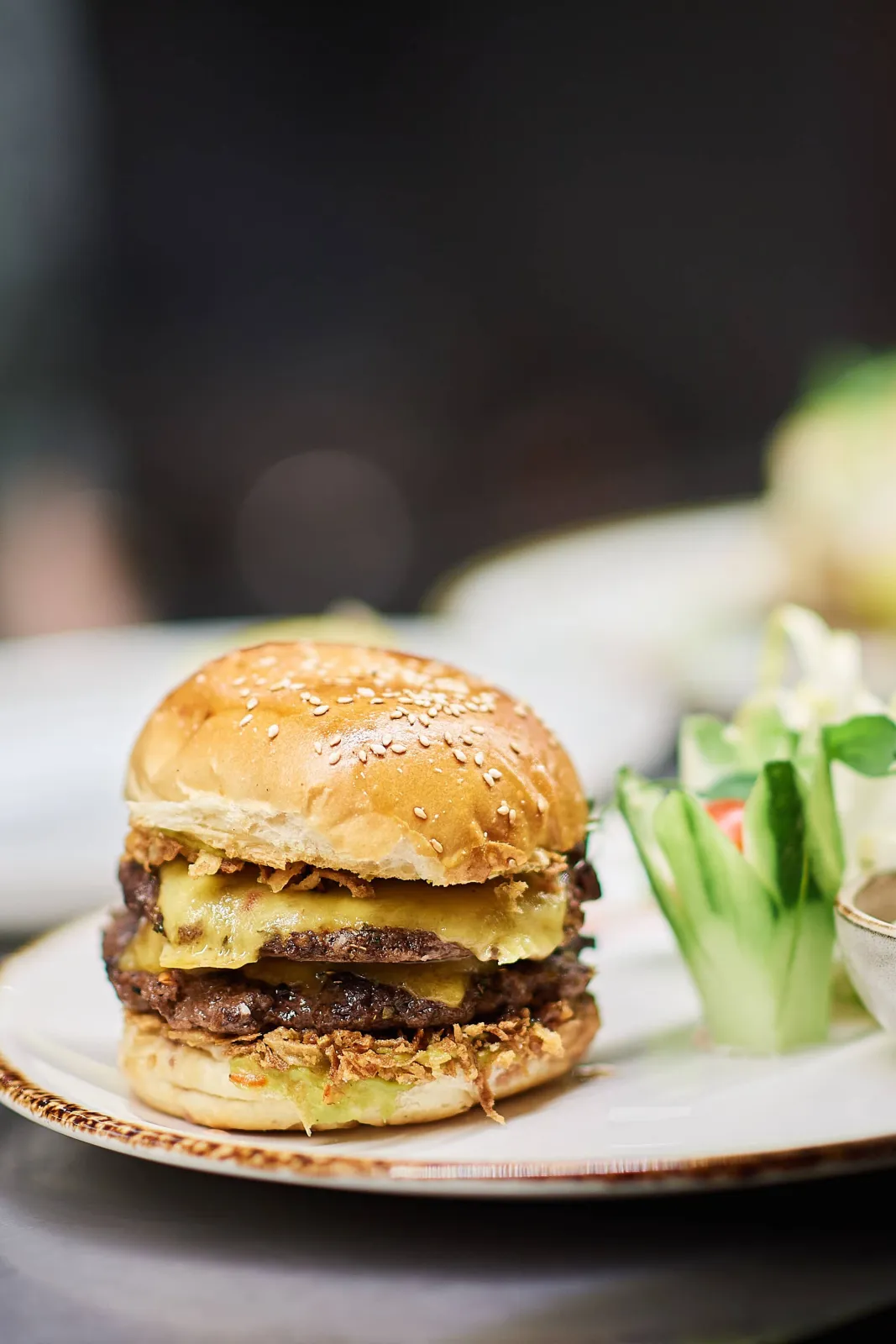 Dubbele cheeseburger met krokante uitjes en komkommer op een bord