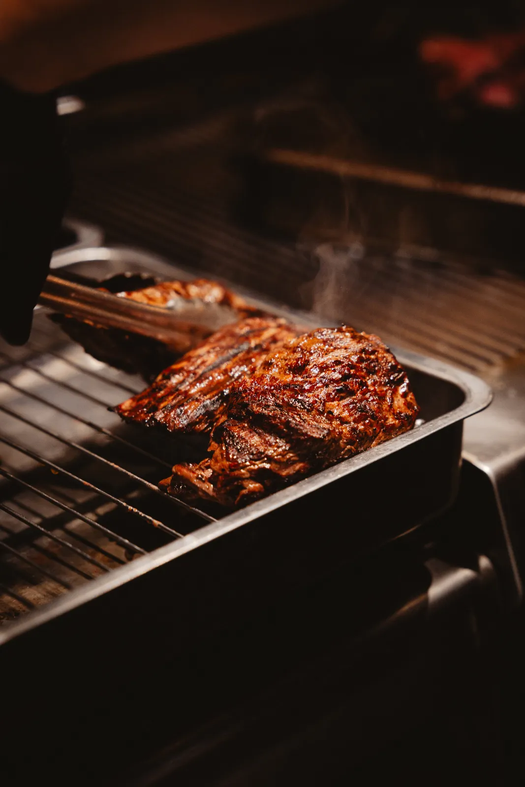 Gegrild stuk rundvlees wordt met een tang op de grill gedraaid
