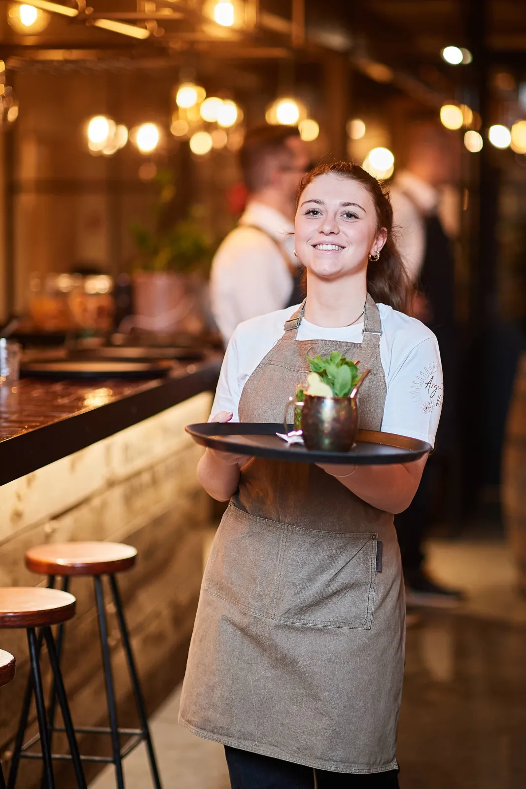 Lachende medewerkster in schort met een cocktail op een dienblad