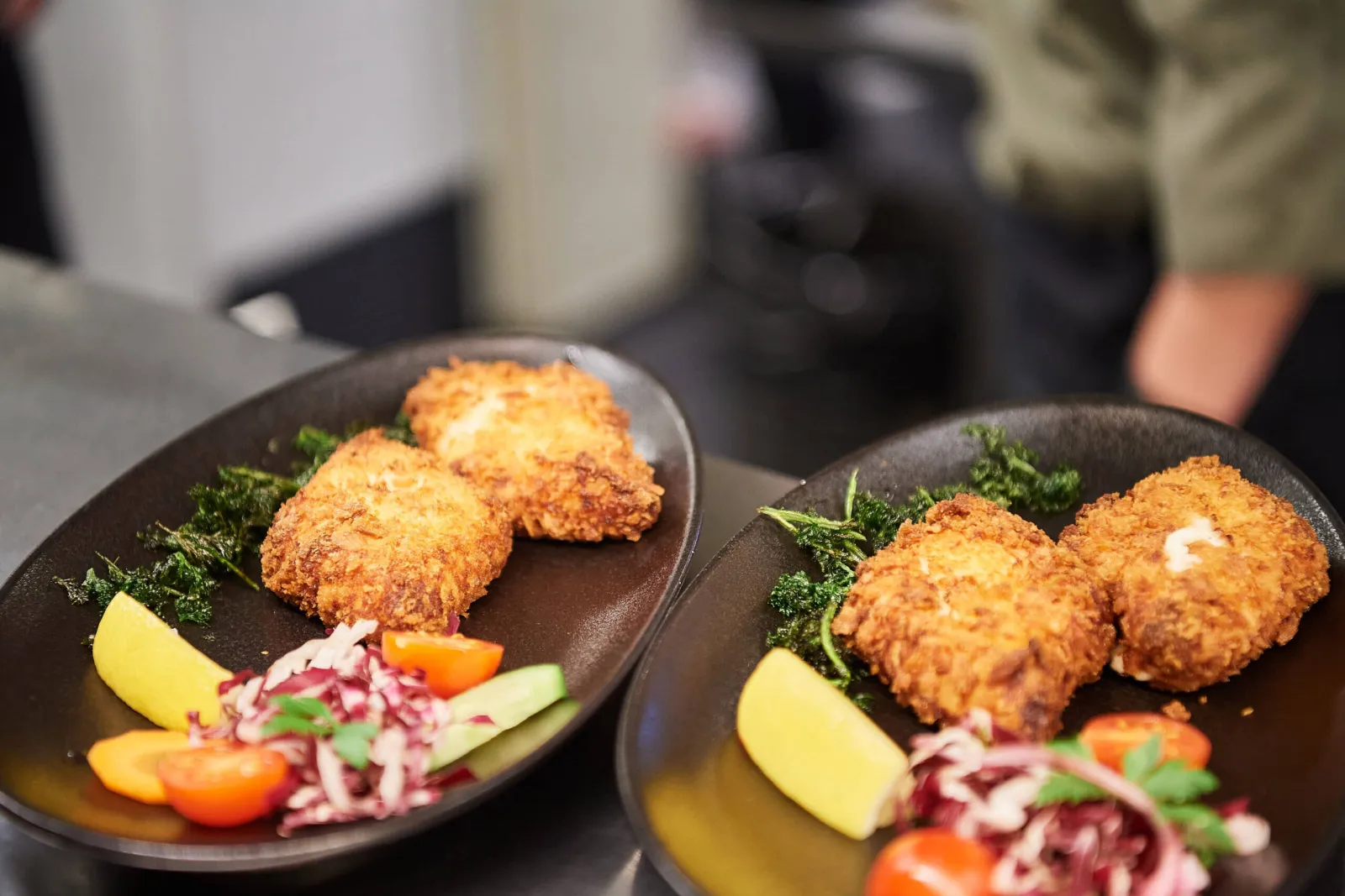 Kroketten met citroen, rodekoolsla en tomaat op twee zwarte borden