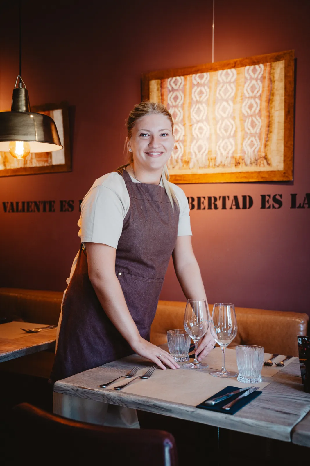 Een medewerkster in schort dekt glimlachend een tafel