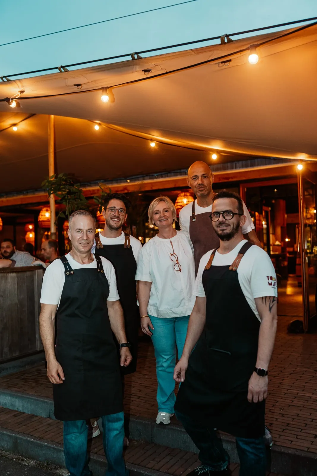 Het team poseert 's avonds voor het overdekte terras met lichtjes